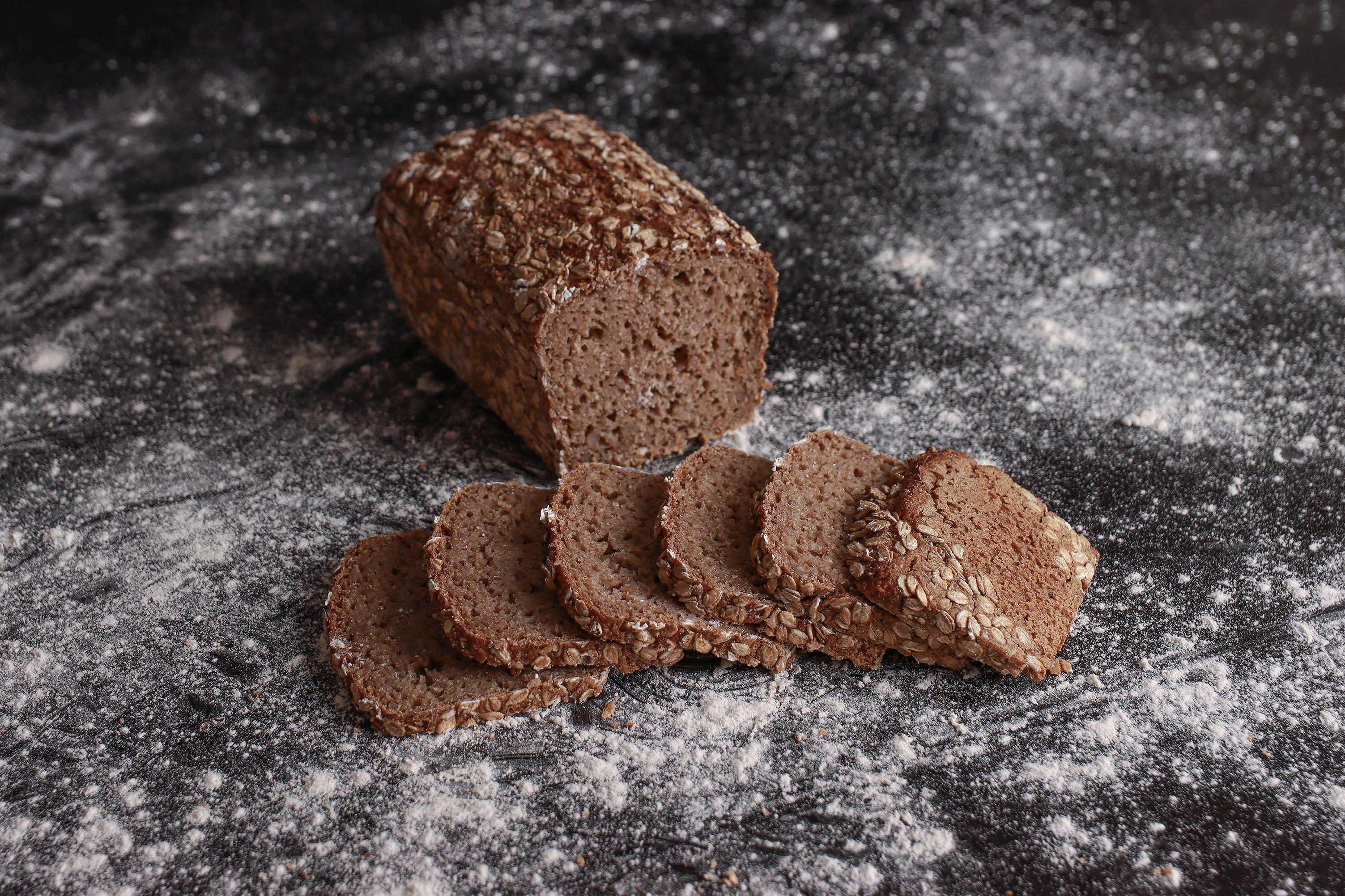 Ein halbes Dinkelbrot liegt aufgeschnitten im Hintergrund. Vorne liegen sechs Scheiben des Brots nebeneinander.