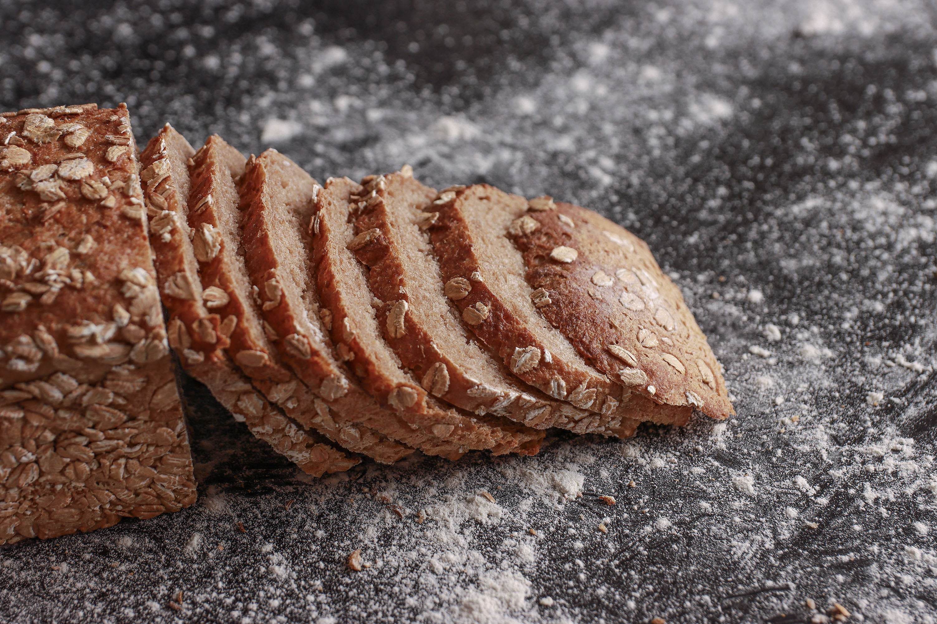 Roggenvollkornrot von der Seite. Sieben Scheiben Brot sind an die andere Hälfte des Brots gelehnt.