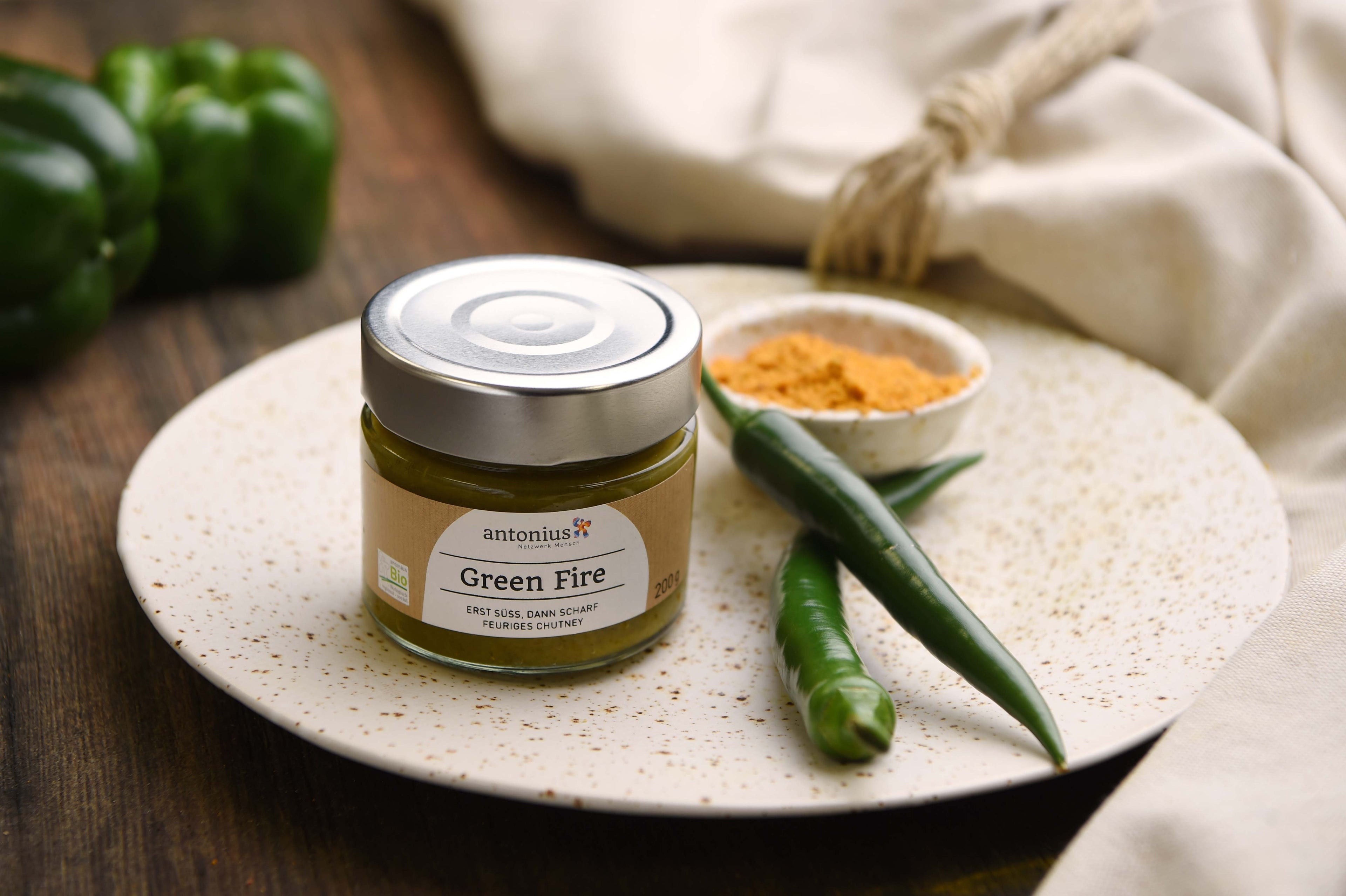 Glas Green Fire Chutney auf einem Teller, dekoriert mit einer grünen Peperoni und Gewürzen.