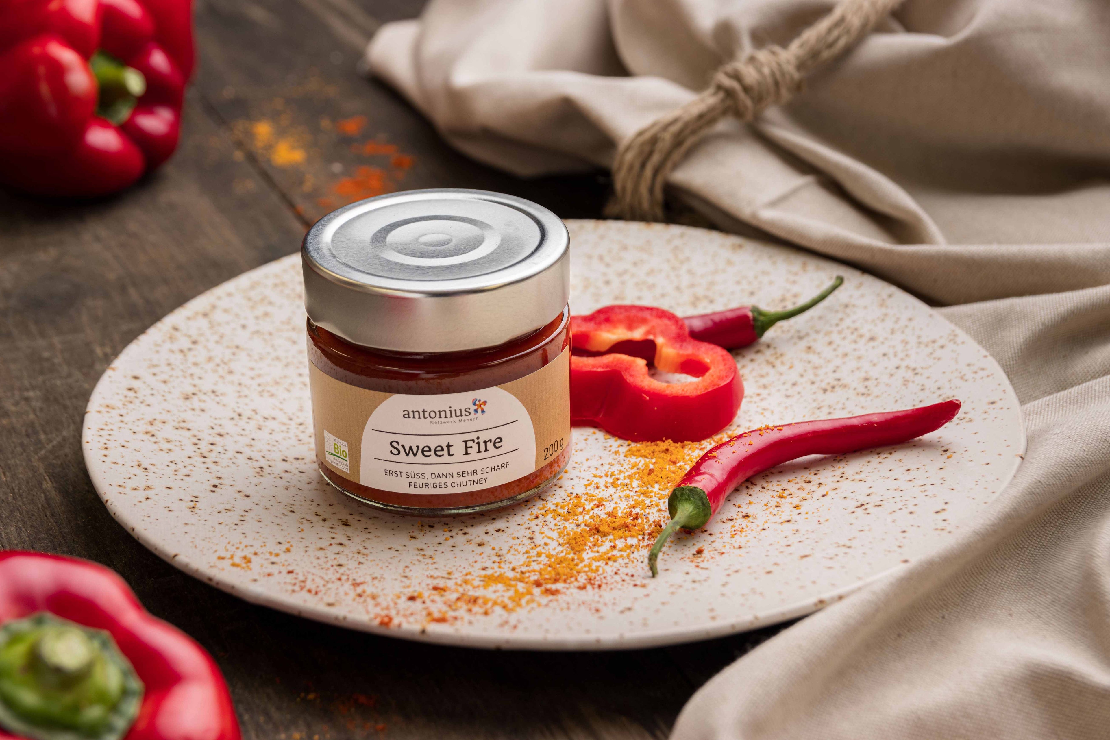 Glas Chutney auf einem Teller mit hübsch angerichteter Paprika und Peperoni als Dekoration.