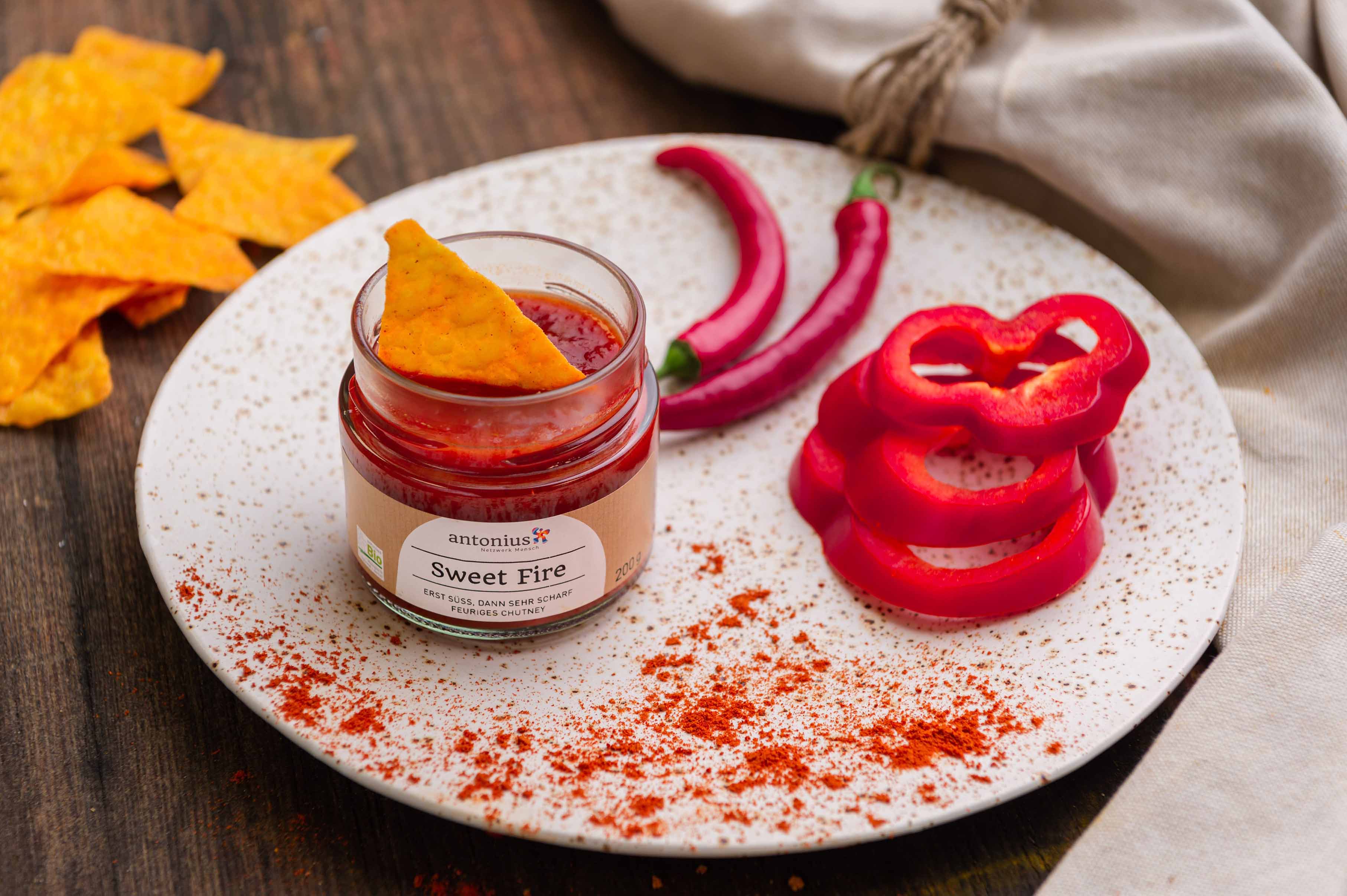 Offenes Chutney auf einem Teller mit hineingetunkten Nachos, dekoriert mit Paprika und Peperoni.