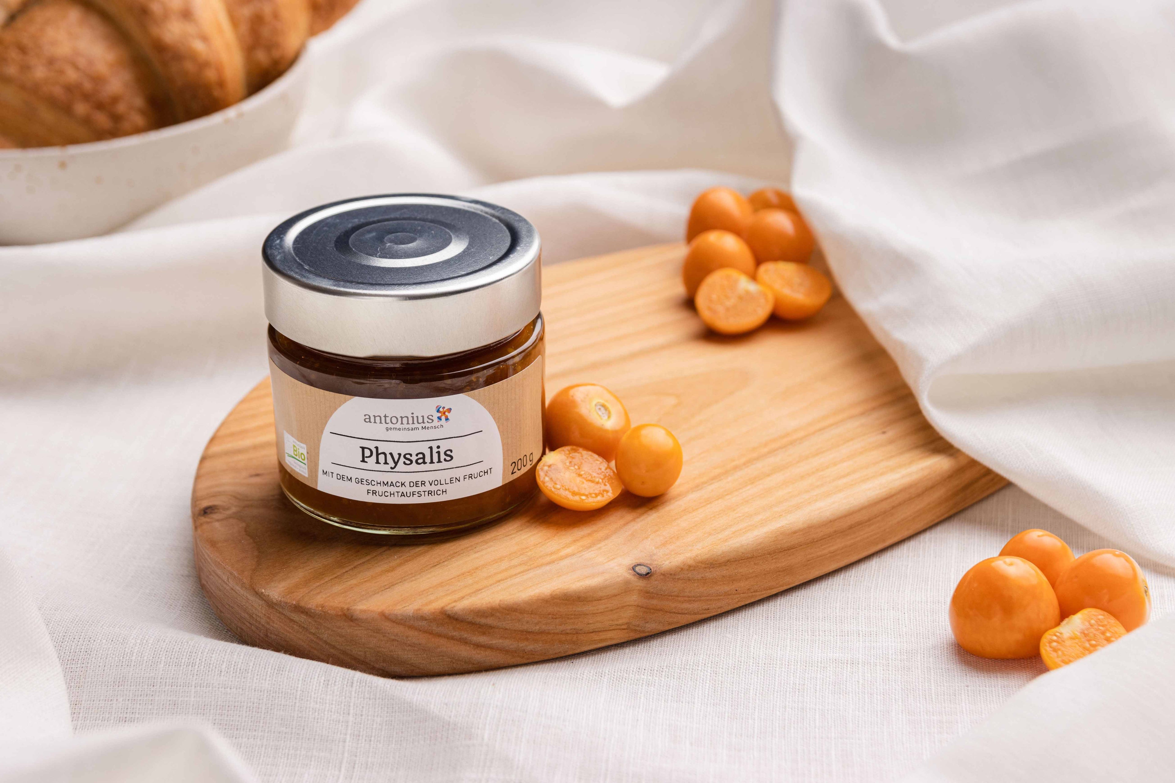 Ein Glas Physalis-Fruchtaufstrich auf einem Frühstücksbrettchen, angerichtet mit Physalis-Früchten.