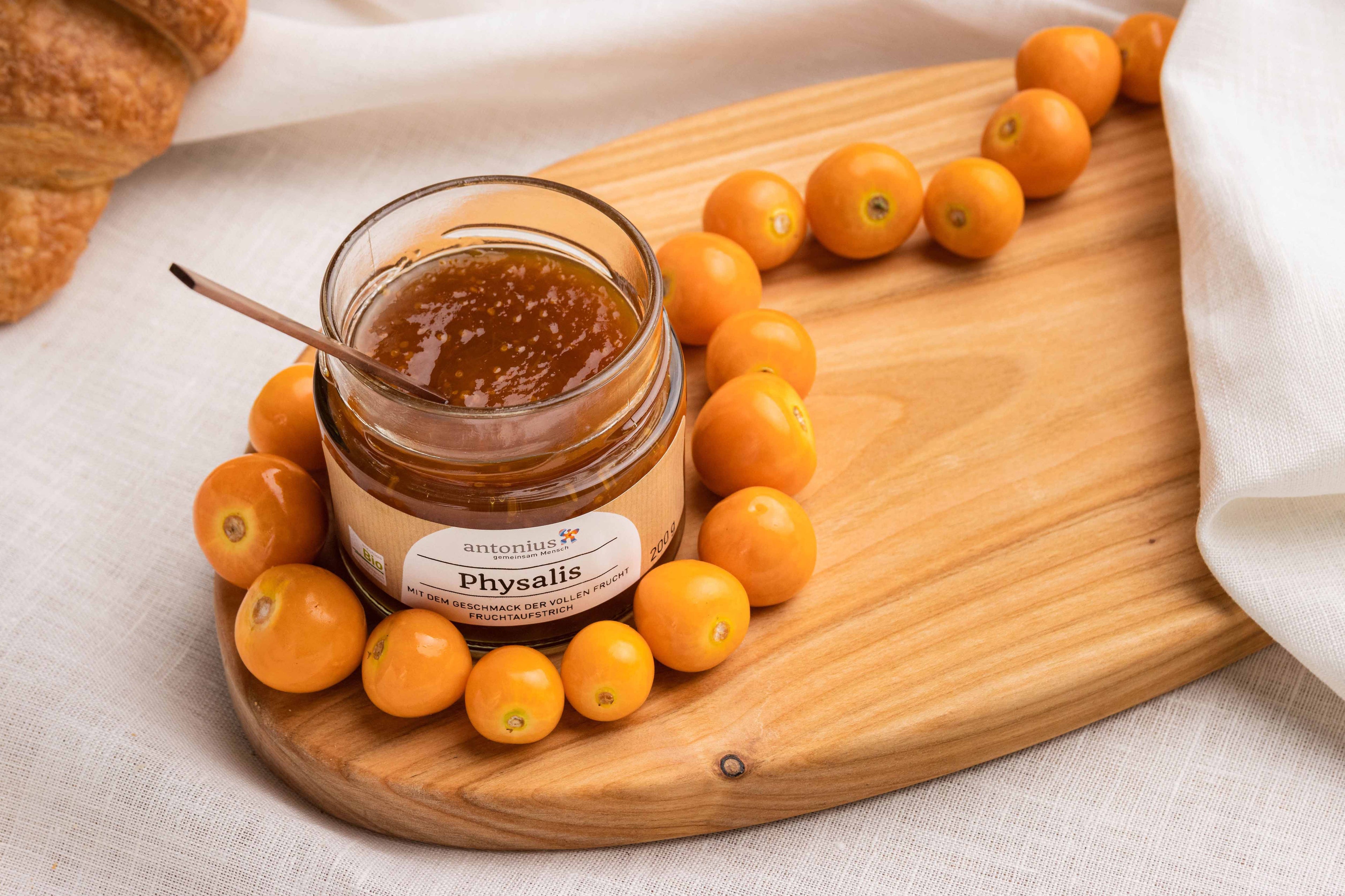 Ein offenes Glas Physalis-Fruchtaufstrich auf einem Frühstücksbrettchen, angerichtet mit Physalis-Früchten.