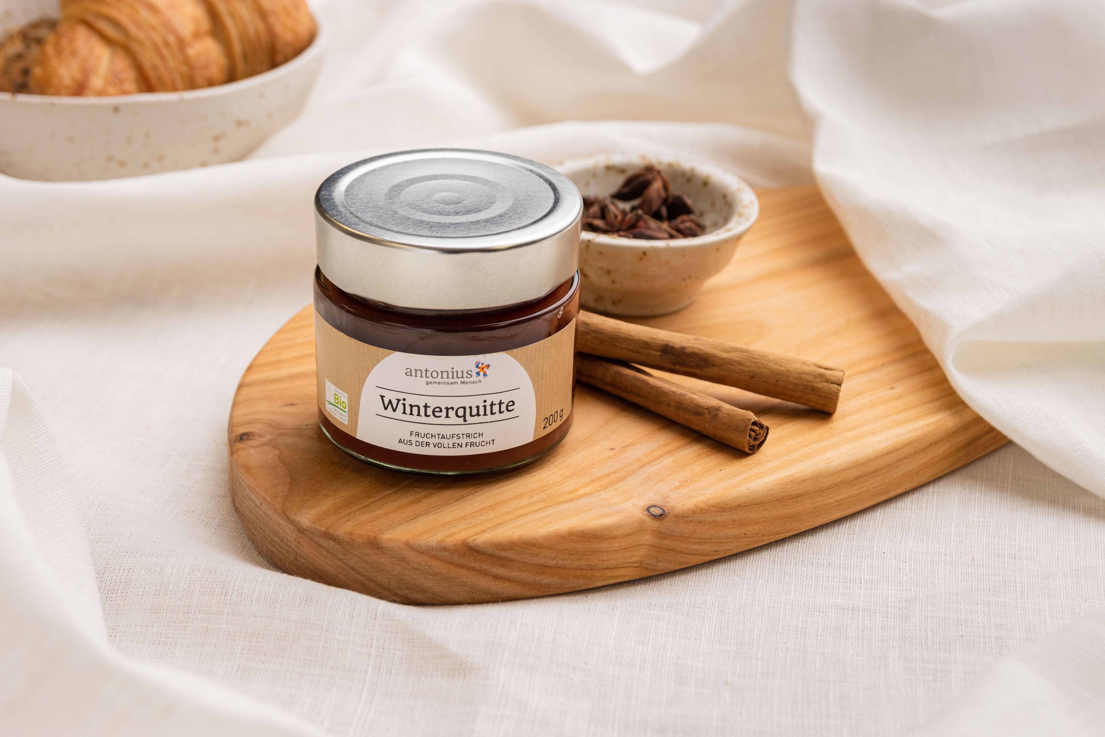 Ein Glas Winterquitten-Fruchtaufstrich auf einem Frühstücksbrettchen, angerichtet mit Nelken und Zimt.