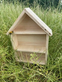 Ein Insektenhotel aus Holz steht auf einer Wiese.