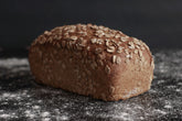 Ein Laib Roggenvollkornbrot in einer Kastenform, bestreut mit Roggenflocken. Gebacken von Hand und in Bio-Qualität in der antonius Bäckerei.