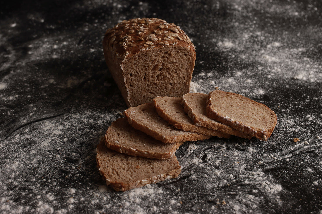 Ein halbes Roggenvollkornbrot liegt aufgeschnitten im Hintergrund. Vorne liegen sechs Scheiben des Brots nebeneinander.