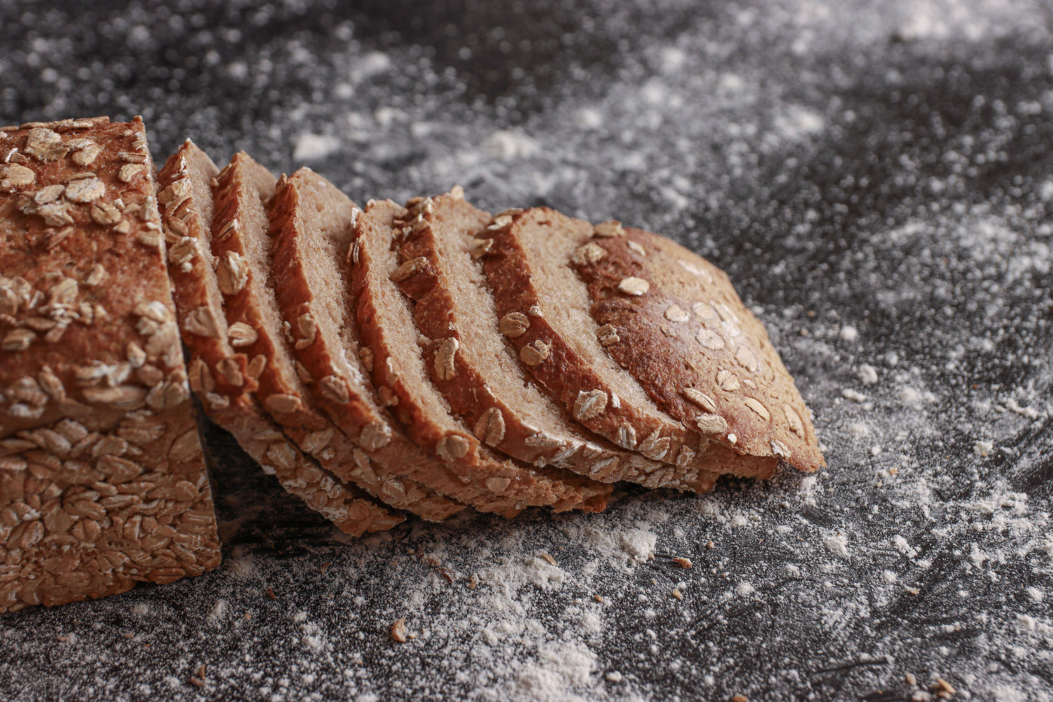 Roggenvollkornrot von der Seite. Sieben Scheiben Brot sind an die andere Hälfte des Brots gelehnt.