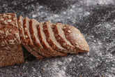 Roggenvollkornrot von der Seite. Sieben Scheiben Brot sind an die andere Hälfte des Brots gelehnt.