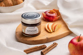 Ein Glas Apfelstrudel-Fruchtaufstrich auf einem Frühstücksbrettchen, angerichtet mit Apfelscheiben und Zimt.