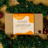 Eine Geschenkkiste aus Pappe und mit einem Streifen aus Papier umbunden. Auf dem Papier kann man antonius, gemeinsam Mensch lesen, sowie Rhöner Winterfeuer Kiste.