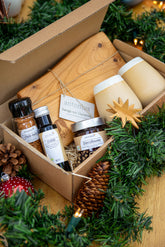 Der Inhalt der Kiste. Gefüllt mit zwei handgemachten Baumassen in Basaltweiß, einem Rhönbrett, einem Stern-Holzanhänger, Chilisalz und Chiliöl und einen Fruchtaufstrich in der Sorte Zimtpflaume. Die Kiste ist gefüttert mit Heu.