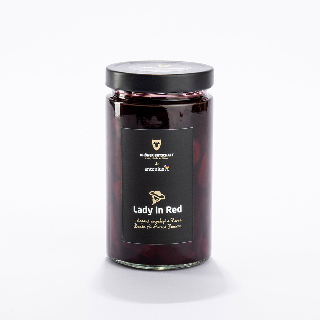 Ein durchsichtiges Einmachglas ist gefüllt mit Roter Bete in dunkelrotem Sud und verschlossen mit einem schwarzen Metalldeckel. Auf dem Etikett steht &quot;Lady in Red ...elegant eingelegte Rote Beete mit Aronia Beeren&quot;.