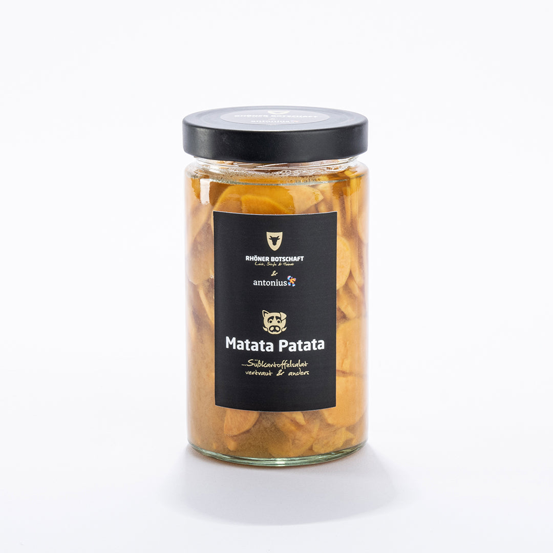 Ein Einmachglas ist gefüllt mit Süßkartoffelscheiben und verschlossen mit einem schwarzen Metalldeckel. Auf dem schwarzen Etikett steht &quot;Matata Patata ...Süßkartoffelsalat vertraut &amp; anders&quot;.