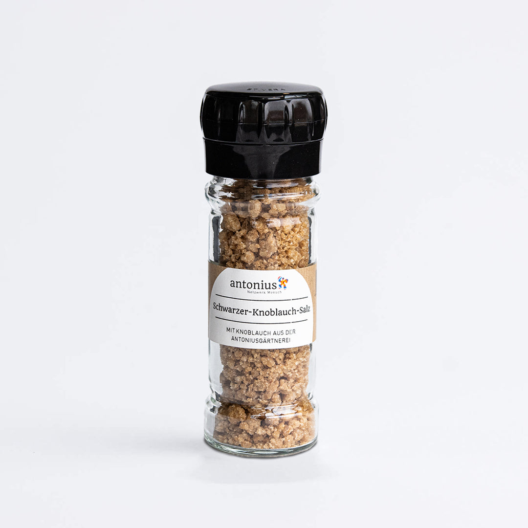 Glasmühle mit Plastikdeckel, gefüllt mit Gewürz, Bioqualität. Besteht aus Meersalz und Knoblauch aus ökologischem Anbau. Beschriftet mit antonius: gemeinsam Mensch, Schwarzer-Knoblauch-Salz, mit Knoblauch aus der antoniusgärtnerei.
